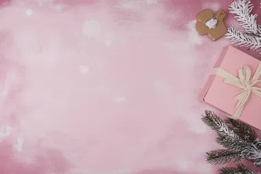 Christmas-themed pink background with white snowflakes, Christmas tree branches, and a gift box on a pastel pink tabletop. Flat lay style. Bright colors, high resolution. The concept of holiday celebration and shopping in the festive season. Stock photo with 2/3 space for text.  --s 50  sqq5bir