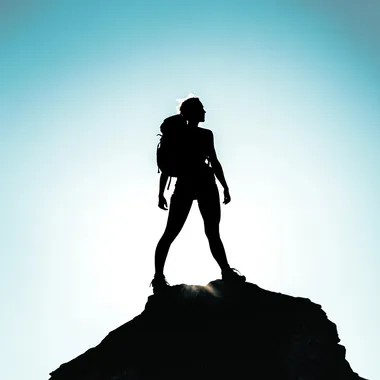 Silhouette of a fit woman standing on top of a peak, minimalist, hiking gear, light and shadows