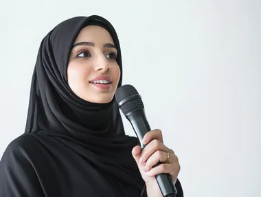 Presenting artistic and singing shows and entertainment segments, an Omani woman giving speeches, the concept of art and its positive impact on women, starting vocal training, a close-up portrait of a young Saudi Arabian Gulf woman wearing an abaya holding a microphone in her hand with gestures of integration into singing, white background